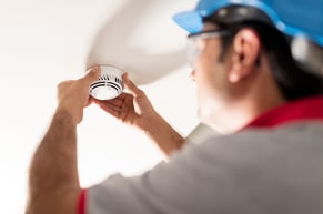 worker performing routine maintenance on a smoke alarm