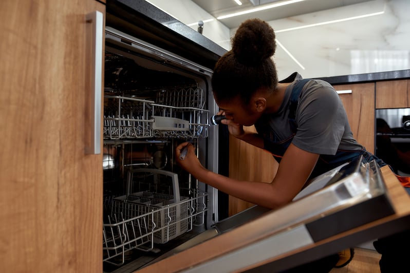 worker completing a corrective maintenance task on a dishwasher