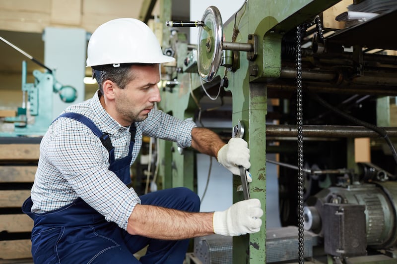 maintenance technician performing routine maintenance while adjusting machinery; inspecting equipment